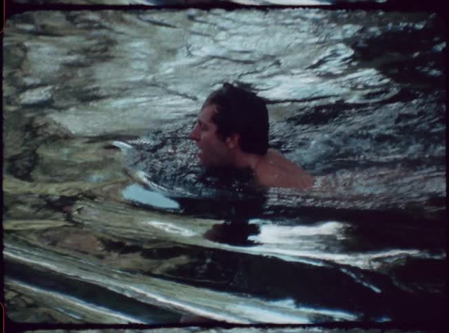 A man swimming under a tree trunk then up to a pier