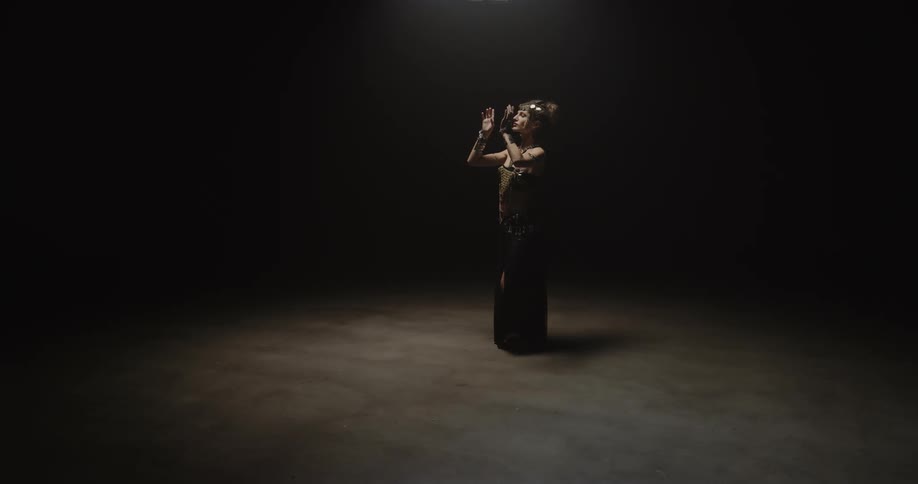 A woman belly dances in a dim room