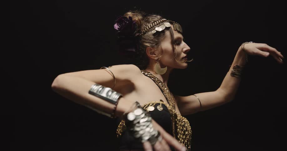 A costumed woman is in a studio environment belly dancing underneath a spotlight in a darkened room