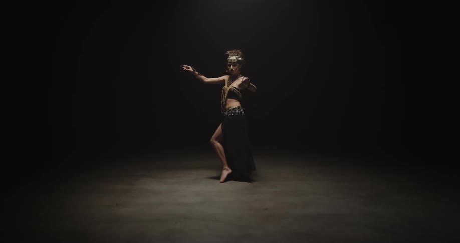Belly dancer wearing bedlahheadbands with golden coins golden necklace and bracelets performs dance on stage