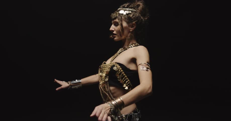 Belly dancer in bedlah headbands with golden coins golden necklace and bracelets performs dance and moves of the hips and torso on stage