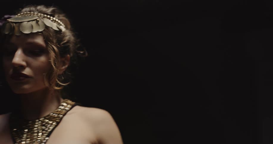 Belly dancer wearing bedlahheadbands with golden coins golden necklace and bracelets performs dance on stage