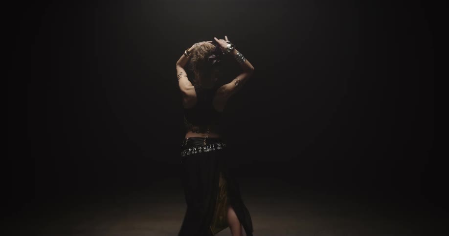 A woman is belly dancing as she moves her arms and body in the darkness