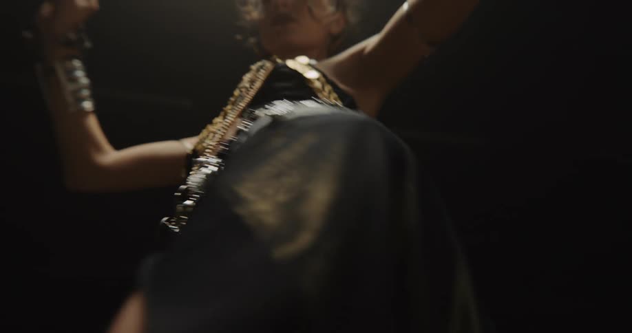 A dancer is belly dancing in full costume in a dark studio
