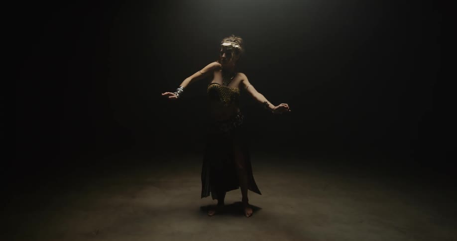 A woman is belly dancing as she moves her arms and body on the stage in the darkness