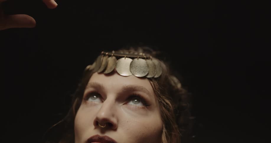 A woman wearing jewelry and a hair accessory waving her hands around slowly while looking upwards