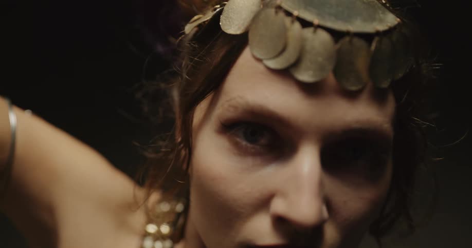 Belly dancer wearing headband with golden coins dances and looks at camera on stage