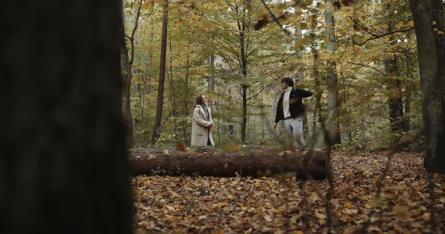 A young man and woman holding hands while walking in a forest in autumn