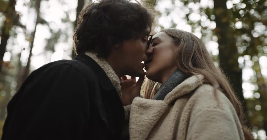 A couple wearing coats kissing in the woods
