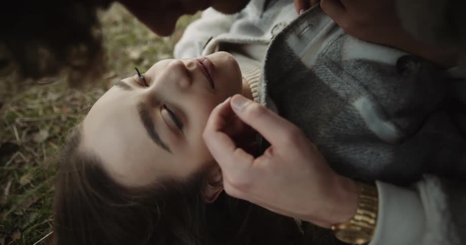 A woman laying on the ground looking up at a man above her making sentimental gestures