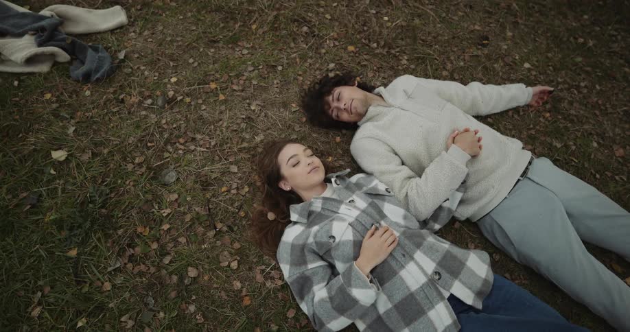 A man and woman laying on the ground holding hands while looking at each other