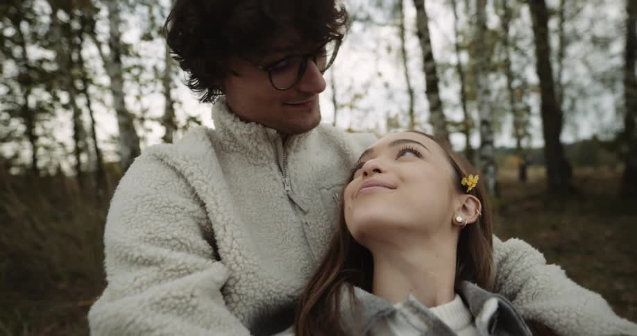 A woman laying in a mans arms while he puts a flower behind her ear then they look at each other sentimentally