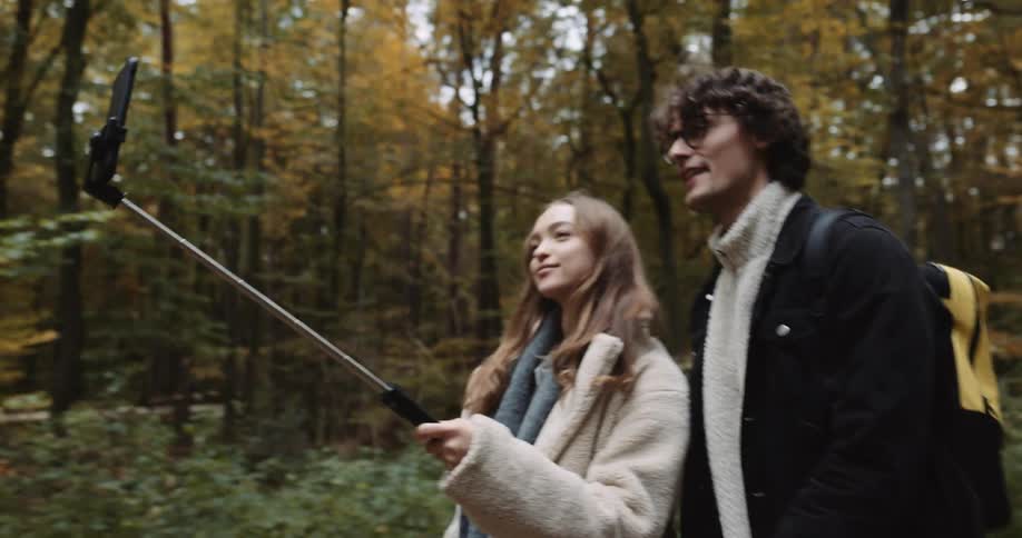 A man and woman record themselves with a selfie stick while walking through the woods