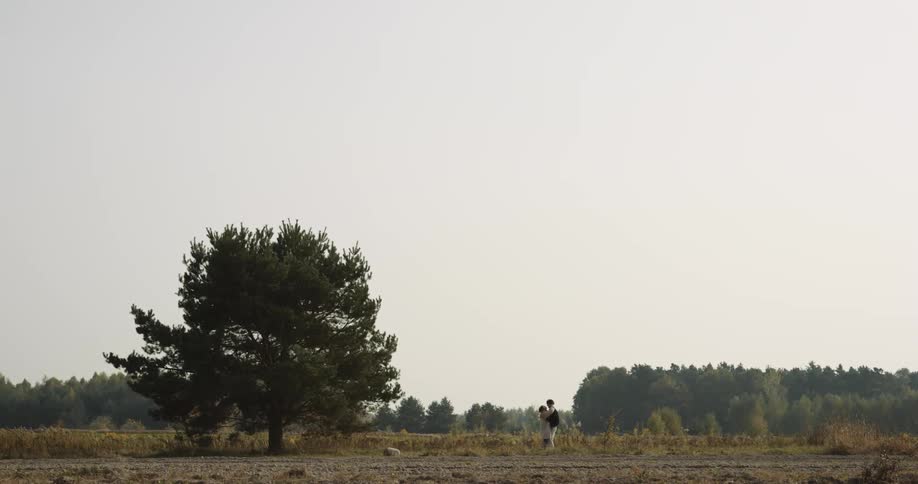 Man and woman run towards each other next to a tree in the field