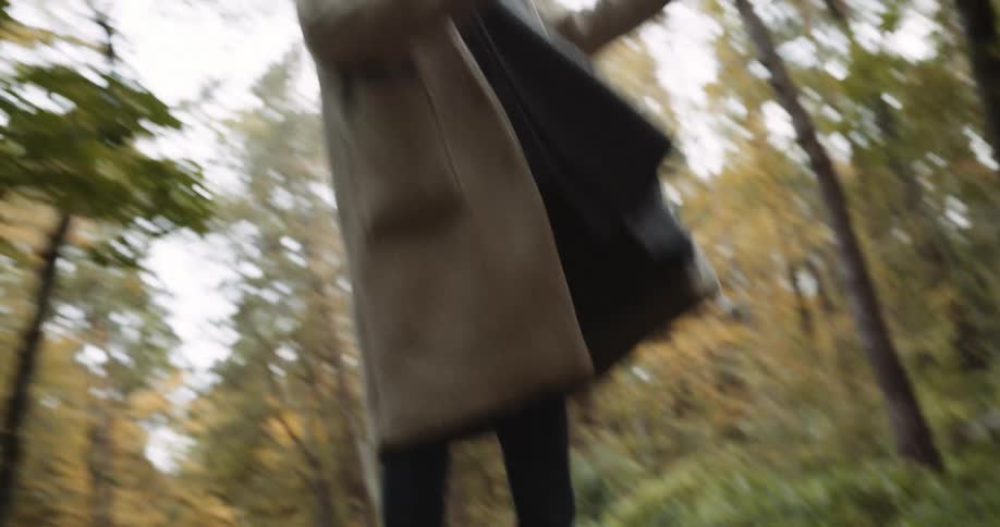 A teenage boy and girl filming themselves on a smartphone while walking in a forested area in autumn