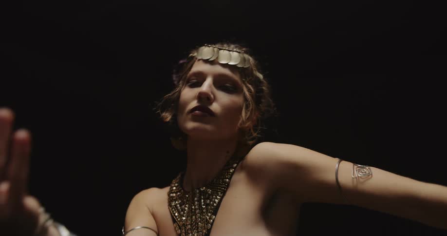 Belly dancer in bedlah headbands with golden coins golden necklace and bracelets performs dance and moves of the hips and torso on stage