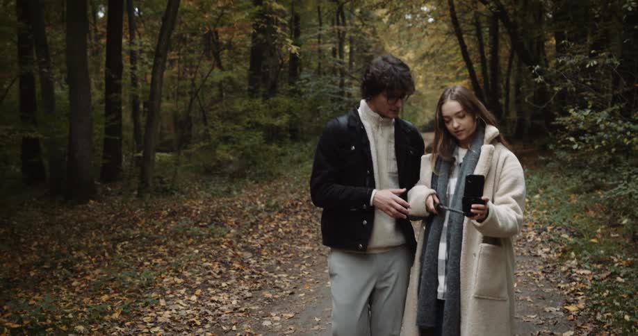 A young couple walking in the woods taking pictures with a phone