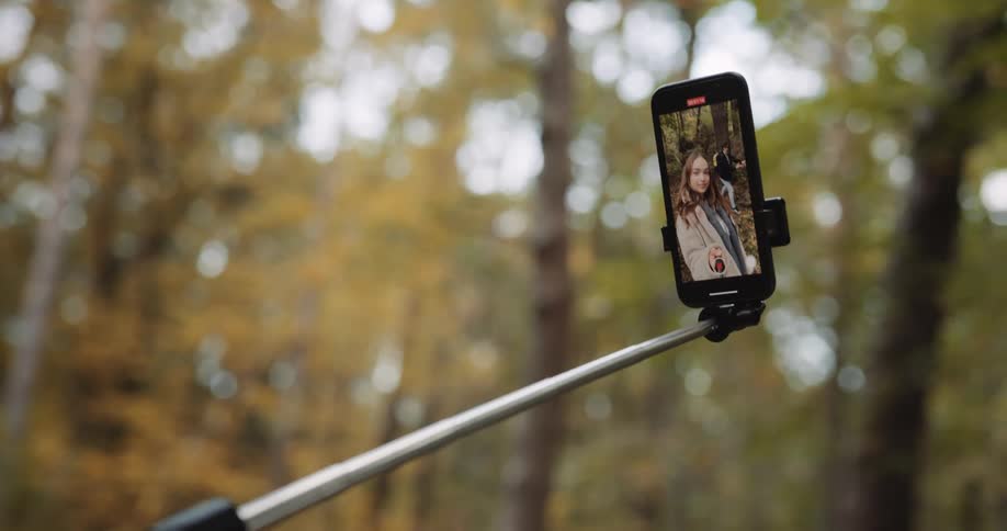 A woman holding a selfie stick with a camera on the end recording herself