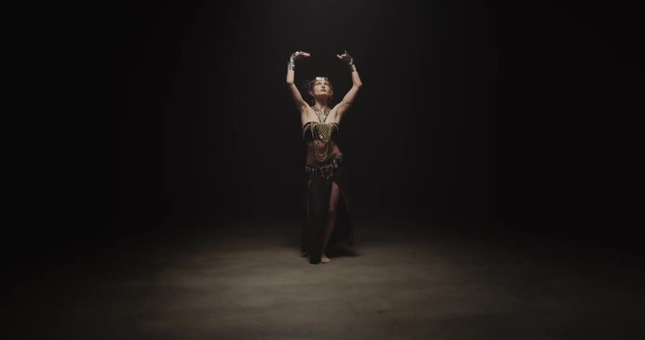 Belly dancer in bedlah headbands with golden coins golden necklace and bracelets performs dance and moves of the hips and torso on stage