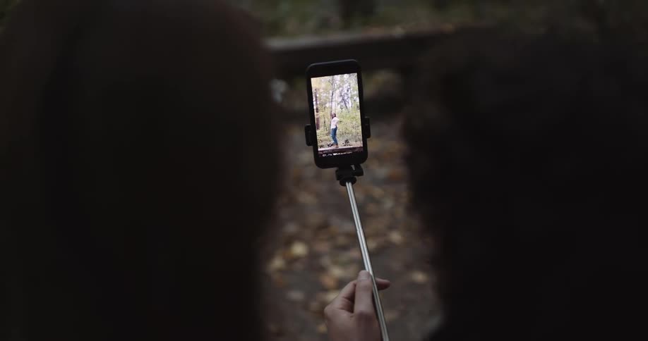 Two women watching a video on a cell phone attached to a selfie stick