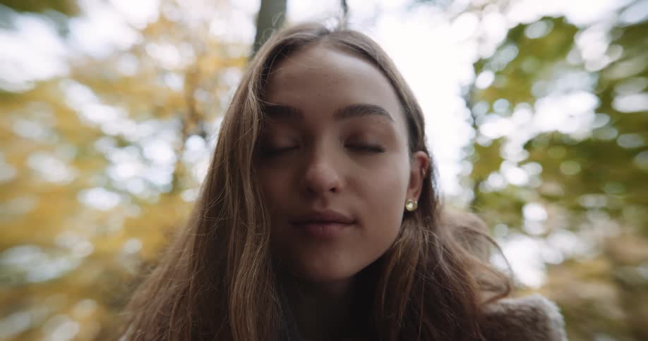 A teenage girl smiling outside near trees with fall foliage