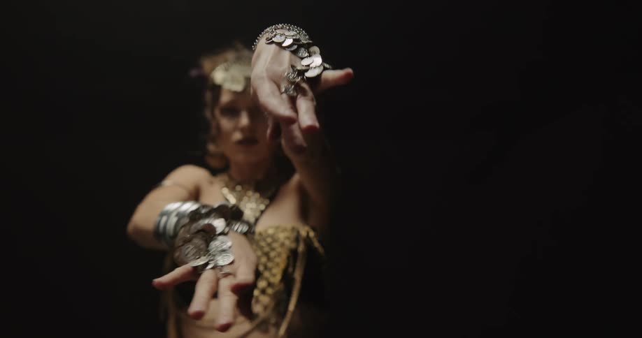 Belly dancer in bedlah headbands with golden coins golden necklace and bracelets performs dance and moves of the hips and torso on stage