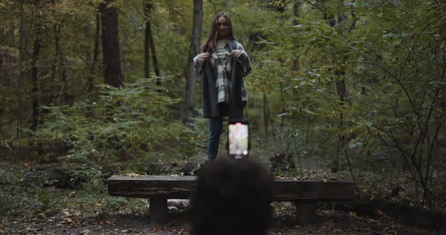 A male taking photos of a female on a bench in the woods