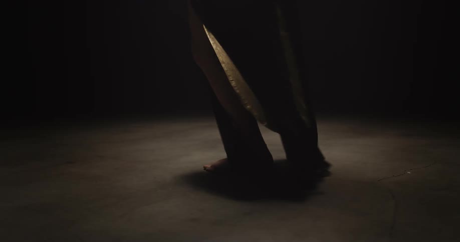 Light shines on a woman as she dances on stage barefoot and her legs move out of her gown