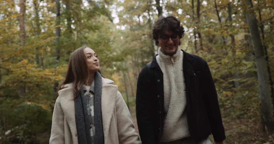A teenage couple are holding hands as they walk through the woods talking and laughing