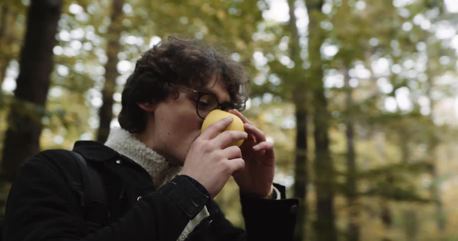 A woman unscrews the cap of a thermos and pours her friend a drink before they walk down a wooded path