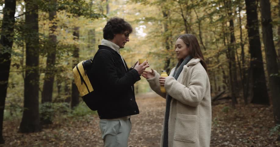 A woman and a man walking through the forest stopping to drink water out of a yellow water bottle
