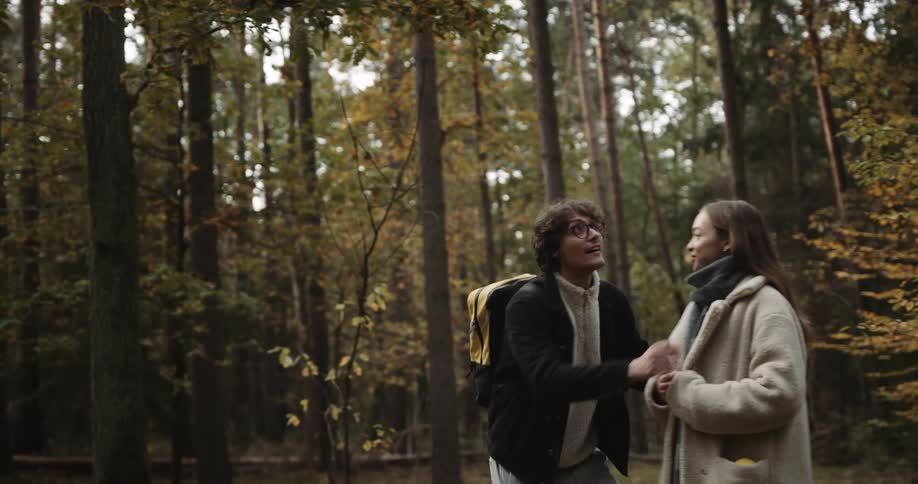 A teenage couple are hiking through the woods and looking at trees