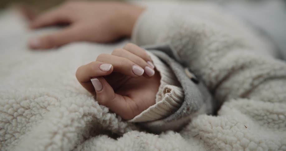 A teenage boy is lying on the ground with his hand on his coat and his girlfriend is lying next to him with her arm under his arm