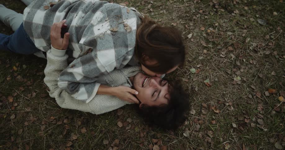 Couple lie together on ground then smile as they kiss and cuddle