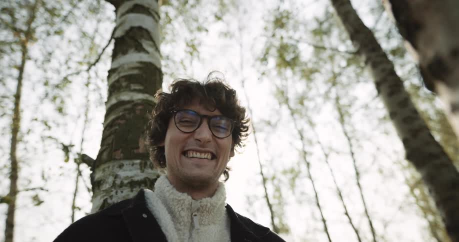 A man is smiling outdoors in a forest area