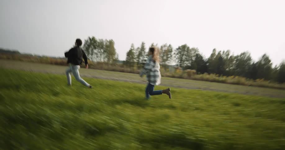 A teenage couple are running and playing chase in a field and they embrace and hug