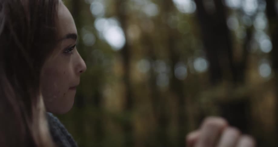A woman is smiling outdoors in a forest area