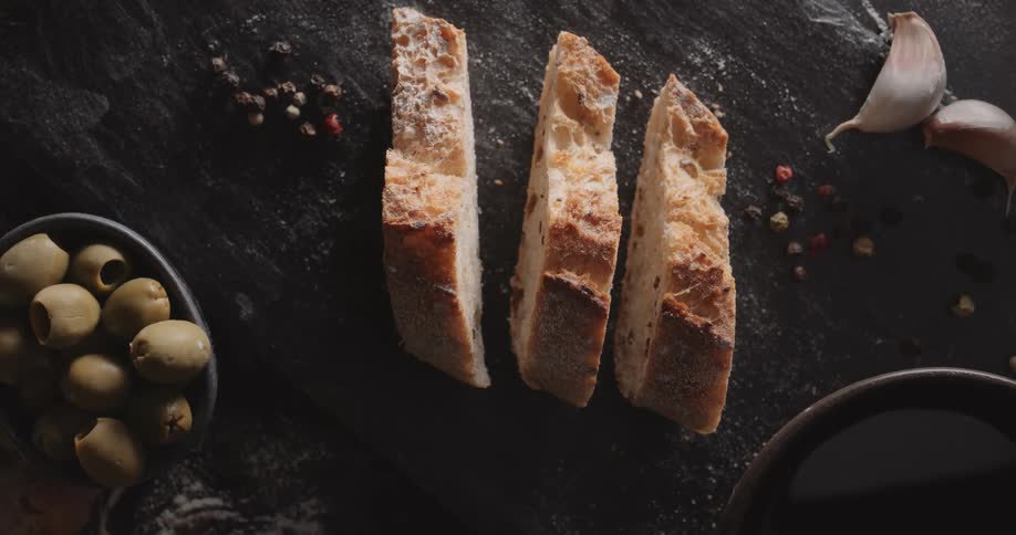 Close up of a loaf of white sliced bread next to olives and garlic on wood