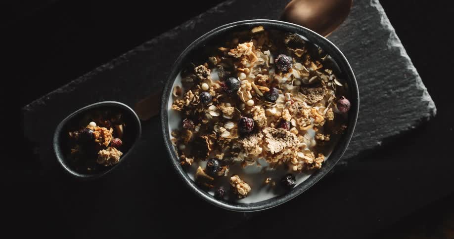 An up close of granola in a bowl with milk and a bronze spoon next to the bowl