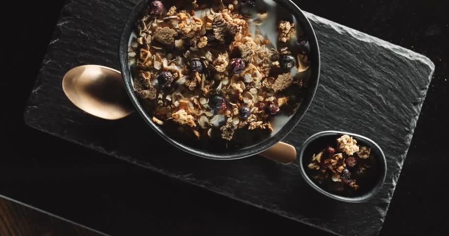 A bowl of granola resting next to a spoon on a table