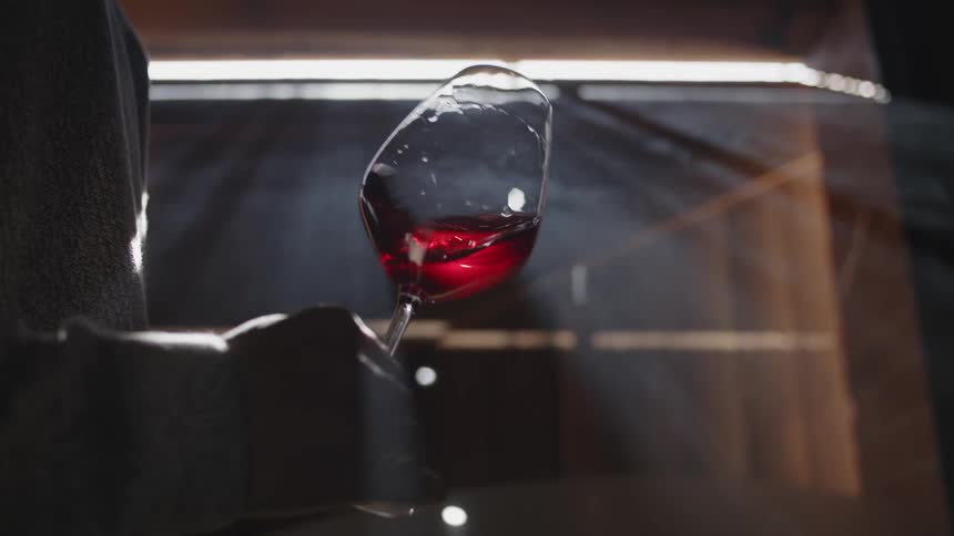 Person stand near opening allowing sunlight to enter swirls wine in glass