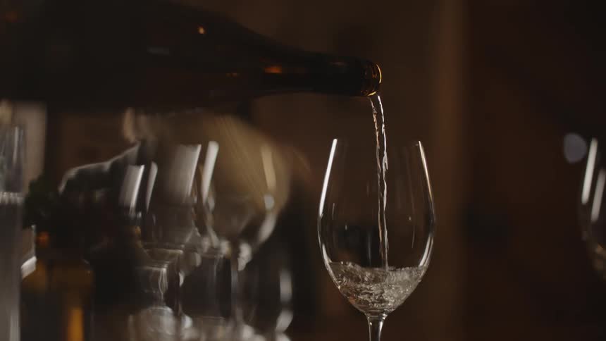 A woman watches as wine is poured into a glass along a counter