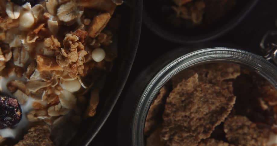 Two bowls of cereal and a jar of cornflakes are all partially shown grouped together on a table