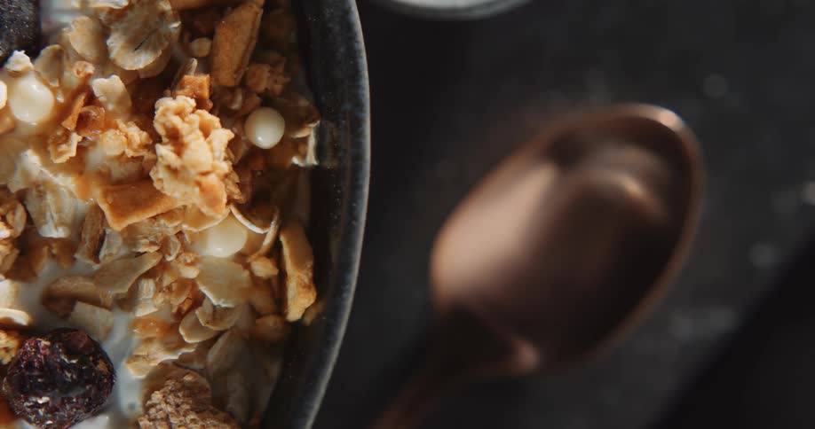 A partial bowl of cereal sits on a table with a metal spoon next to it