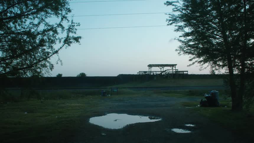 Puddle sits near trash with structure on hill in the background