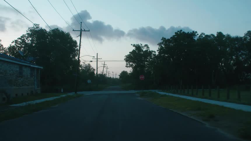 Traveling on a neighborhood street past houses and trees and stopping at the intersection