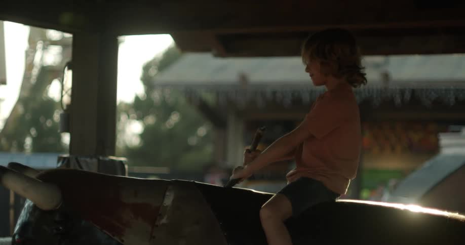 A young boy riding a mechanical bull outside at a fair