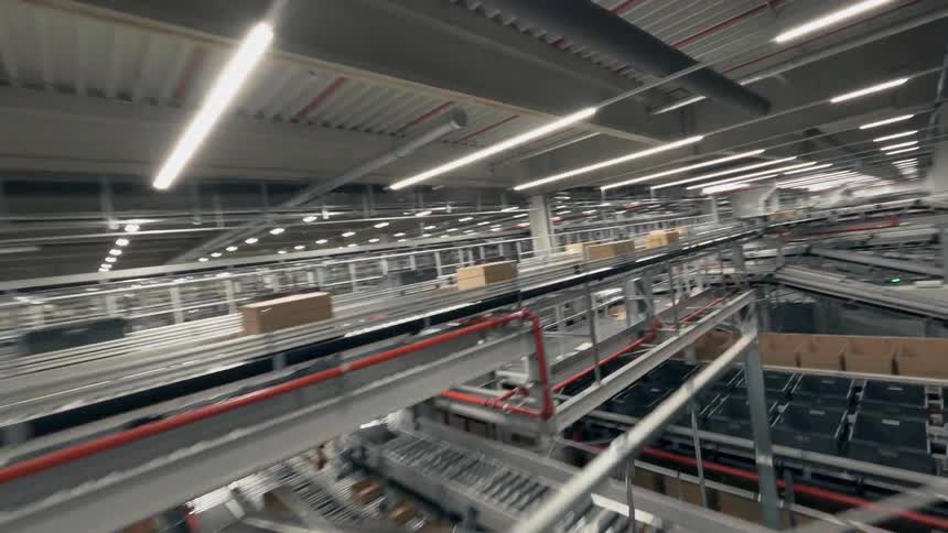 An FPV Drone Races Over and Through a Maze of Automated Conveyor Belts Transporting Boxes Through a Large Warehouse or Distribution Center