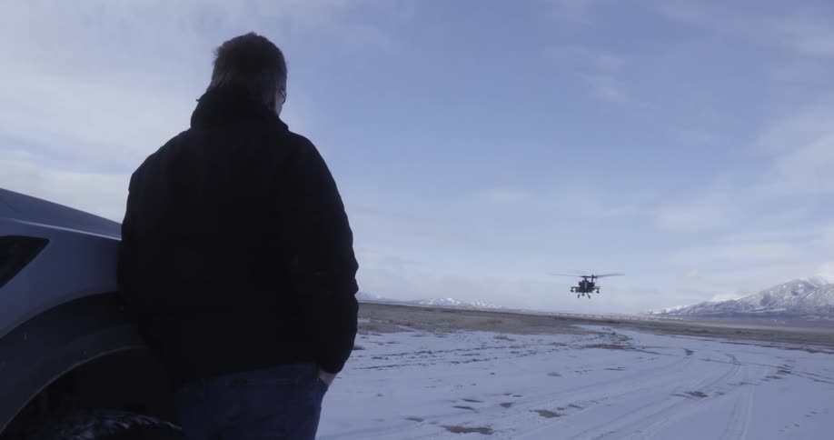 Helicopter flies over man man reclined on a truck in snowy tundra