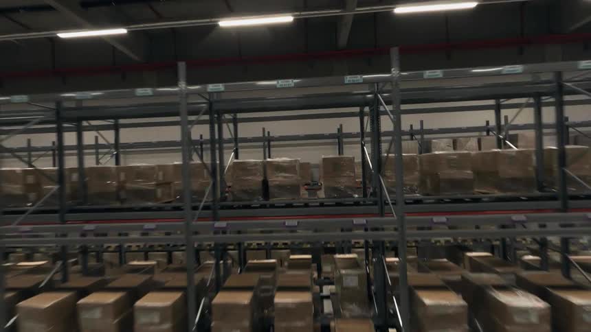 An FPV drone shot that zooms over a forklift and weaves through huge metals racks full of shipping boxes